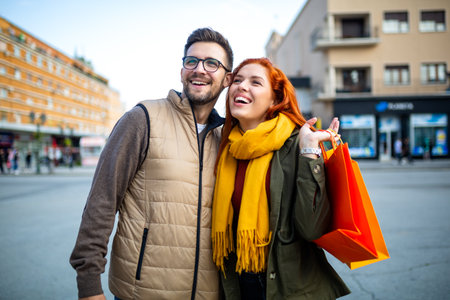 Smiling couple enjoying having fun walking and exploring city street during the day with shopping bagsの写真素材