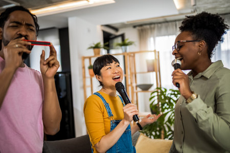 Multiracial group of friends having karaoke night. Singing in to the microphone, drinking beer and playing mouth organ.の写真素材