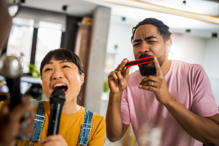 Multiracial group of friends having karaoke night. Singing in to the microphone, drinking beer and playing mouth organ.の写真素材