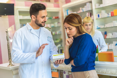 Cheerful pharmacist chemist man giving vitamins, antibiotics to young woman in modern pharmacy.の写真素材