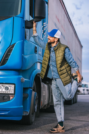 Tired male driver standing in front of his truck and streching out after a long driveの写真素材