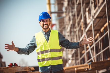 Construction site manager standing  wearing safety vest and helmet, thinking at construction site. Young architect watching construction site with confidence.の写真素材