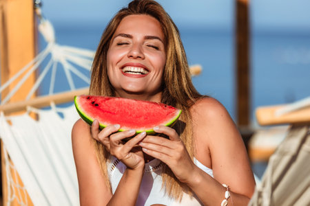 Young beautiful woman eating juicy watermelon on the beach.の写真素材