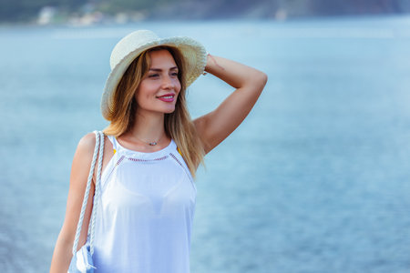 Happy young beautiful woman walking alone on the beach with beach bag and hat.の写真素材