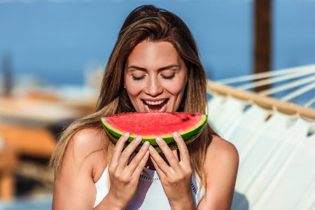 Young beautiful woman eating juicy watermelon on the beach.の写真素材