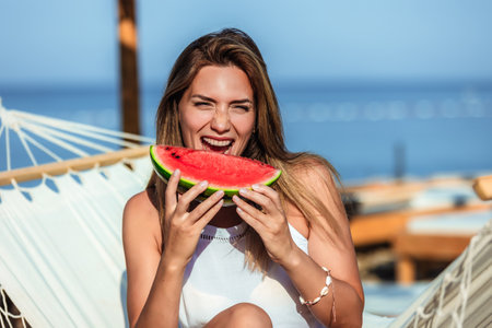 Young beautiful woman eating juicy watermelon on the beach.の写真素材
