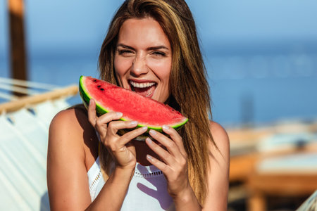 Young beautiful woman eating juicy watermelon on the beach.の写真素材