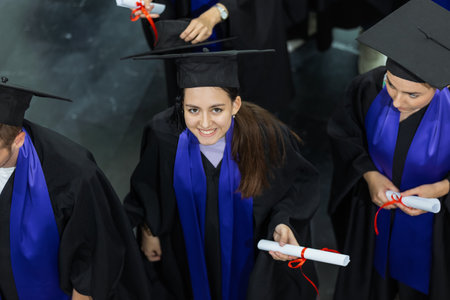 Group of graduates with togas and diplomas standing happy in the hall and looking at the camera.の写真素材