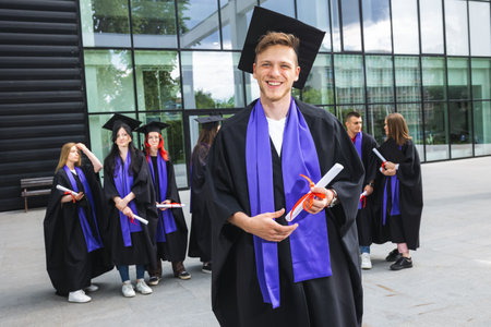 Portrait of graduate student standing in front of his friends with toga and diploma all happy.の写真素材