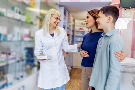 Cheerful pharmacist chemist man giving vitamins to young mom with son in the modern pharmacy.の写真素材