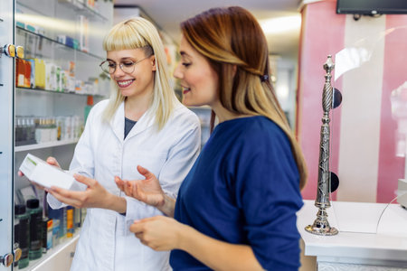 Cheerful pharmacist chemist woman giving vitamins, antibiotics to young woman in modern pharmacy.の写真素材