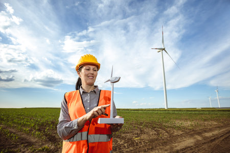 Woman engineer looking at wind turbine farm. She is wearing florescent vest and helmet for protection.の写真素材