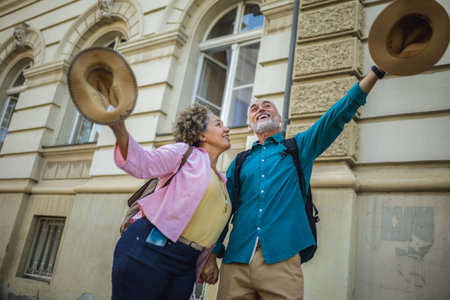 Elderly married couple standing happy in the city center. Throwing hats in the air.
