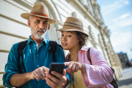 Elderly married couple explores new city. Using their phone for navigation and maps. They are wearing hats and backpacks.の写真素材