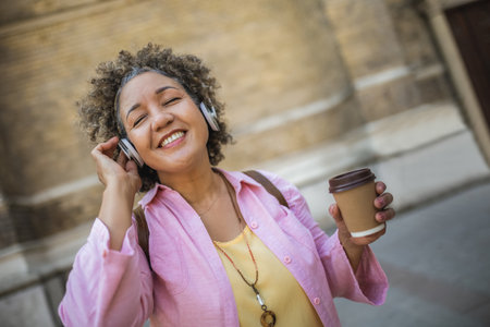 African American older woman wearing headphones in the city center. Wearing headphones and drinking coffee.の写真素材
