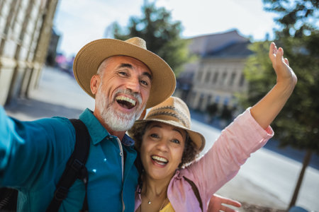 Elderly married couple exploring new city. Taking selfie in the centre. They are wearing hats and backpacks.の写真素材