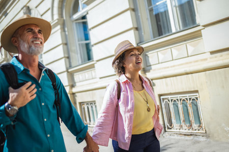 Elderly married couple exploring new city. They are wearing hats and backpacks.の写真素材