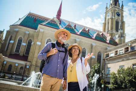 Elderly married couple walking through city center. Impressed with the city. They are wearing...