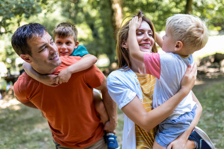 Family of four bonding in the park. Mother and father hugging with their sons.