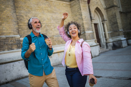 Older mixed married couple having headphones on. They are drinking coffee and dancing to the music. Exploring and traveling concept.の写真素材