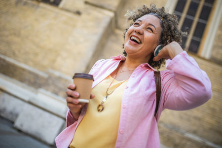 African American older woman wearing headphones in the city center. Wearing headphones and drinking coffee.の写真素材