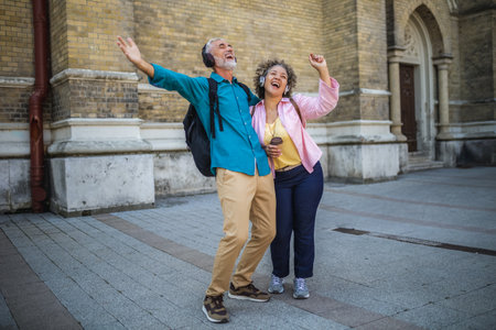Older mixed married couple having headphones on. They are drinking coffee and dancing to the music. Exploring and traveling concept.の写真素材