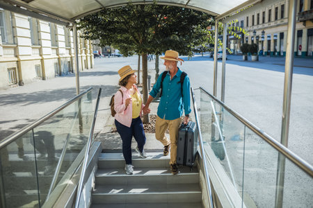 Mature married couple walking down the stairs, entering metro with luggage.の写真素材