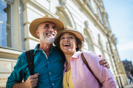 Old married couple exploring the city. Hugging each other. They are wearing hats and backpacks.の写真素材