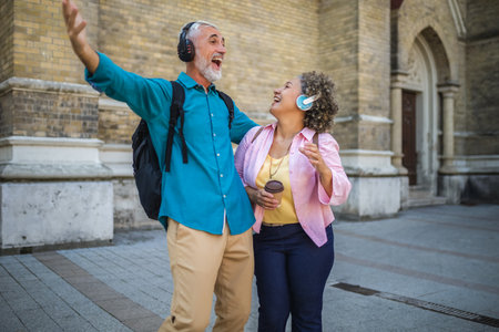 Older mixed married couple having headphones on. They are drinking coffee and dancing to the music. Exploring and traveling concept.の写真素材