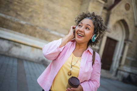 African American older woman wearing headphones in the city center. Wearing headphones and drinking coffee.の写真素材