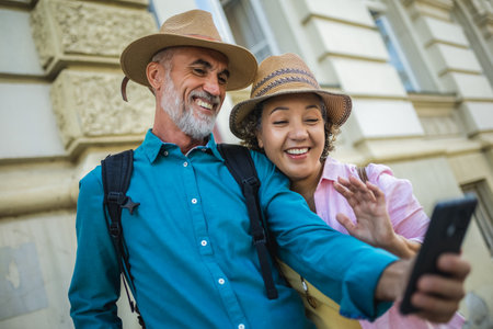 Senior couple explores new city. Using their phone for navigation and maps. They are wearing hats and backpacks.の写真素材