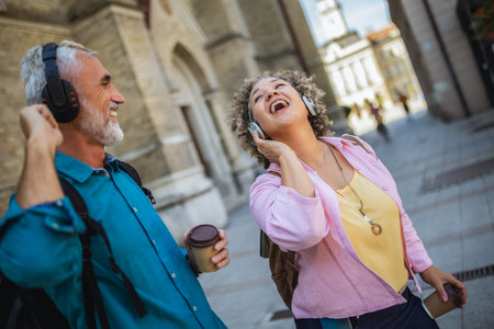 Older mixed married couple having headphones on. They are drinking coffee and dancing to the music. Exploring and traveling concept.の写真素材