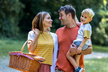 Family of three going on a picnic in the park. They are holding basket, blanket and food.の写真素材