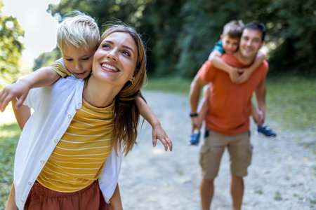 Mother and father with their sons playing in the park. They are carrying them on their back.の写真素材
