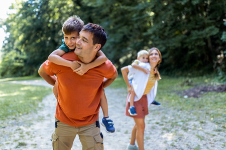 Mother and father with their sons playing in the park. They are carrying them on their back.の写真素材