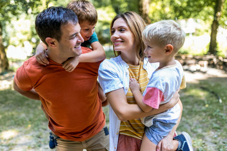 Family of four bonding in the park. Mother and father hugging with their sons.の写真素材