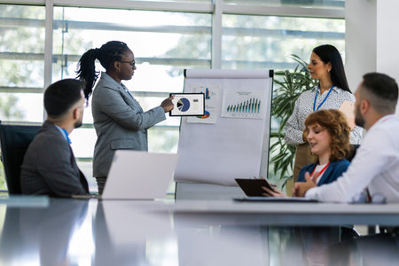 Two businesswoman talking on a meeting in an office with other colleagues. Showing graphics, diagrams and statistics.の写真素材