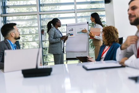Two businesswoman talking on a meeting in an office with other colleagues. Showing graphics, diagrams and statistics.の写真素材
