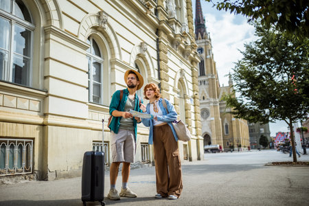 Young couple on a vacation exploring the city. Using the map so they dont get lost. Having suitcases with them.の写真素材