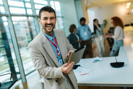 Portrait of young businessman standing in his office in front of his colleagues with tablet in his hands.の写真素材