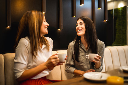Two female friends met at the cafe. Drinking coffee and orange juice. They are talking, gossiping and having fun timeの写真素材