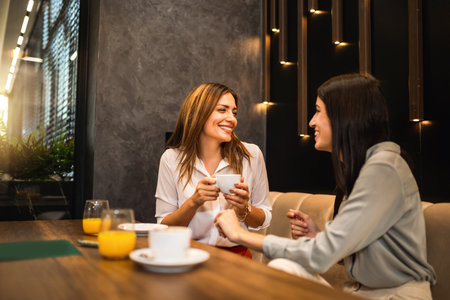 Two female friends met at the cafe. Drinking coffee and orange juice. They are talking, gossiping and having fun time.の写真素材