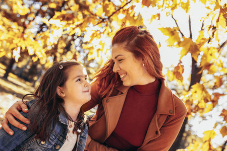 Ginger mom having fun with her daughter in the colorful park. Autumn day.の写真素材