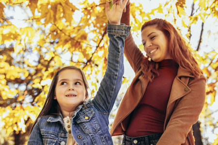 Ginger mom having fun with her daughter in the colorful park. Autumn day.の写真素材