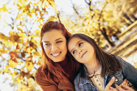Ginger mom having fun with her daughter in the colorful park. Autumn day.の写真素材