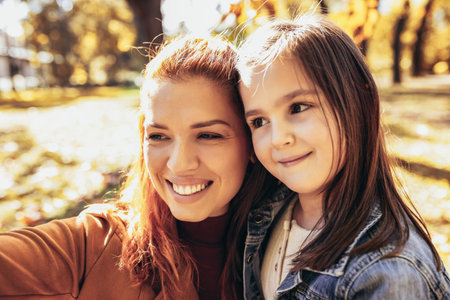 Ginger mom having fun with her daughter in the colorful park. Autumn day.の写真素材