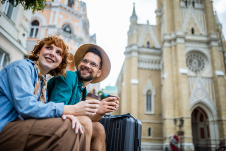 Ginger girlfriend and her boyfriend sitting in the city center and drink coffee. They are on vacation and have their luggages and backpacks with them.の写真素材