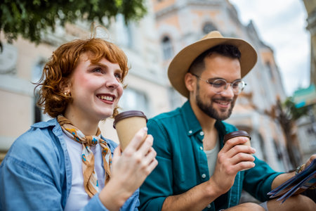 Ginger girlfriend and her boyfriend sitting in the city center and drink coffee. They are on vacation and have their luggages and backpacks with them.の写真素材