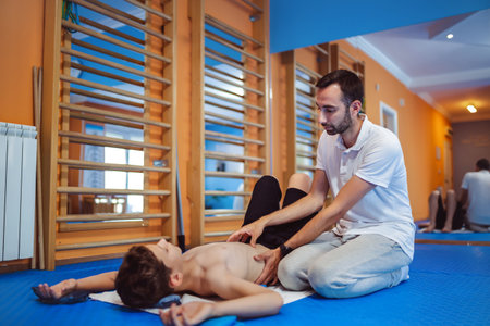 Therapeutic exercise kinesitherapy of little boy. Straightening the spine while the boy is lying down.の写真素材