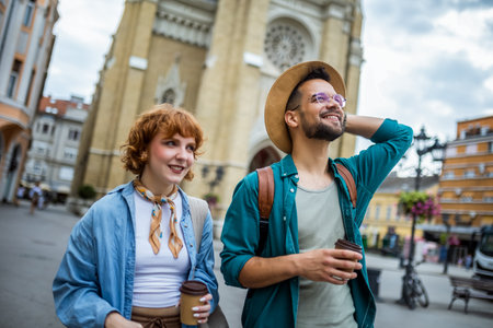 Young couple walking through the new city on their vacation. They are drinking coffee and looking at monuments and buildings.の写真素材